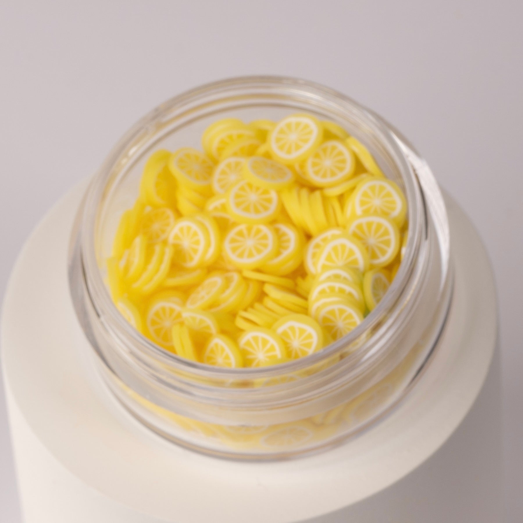 Mini decorative lemon slices in clear jar on white background.