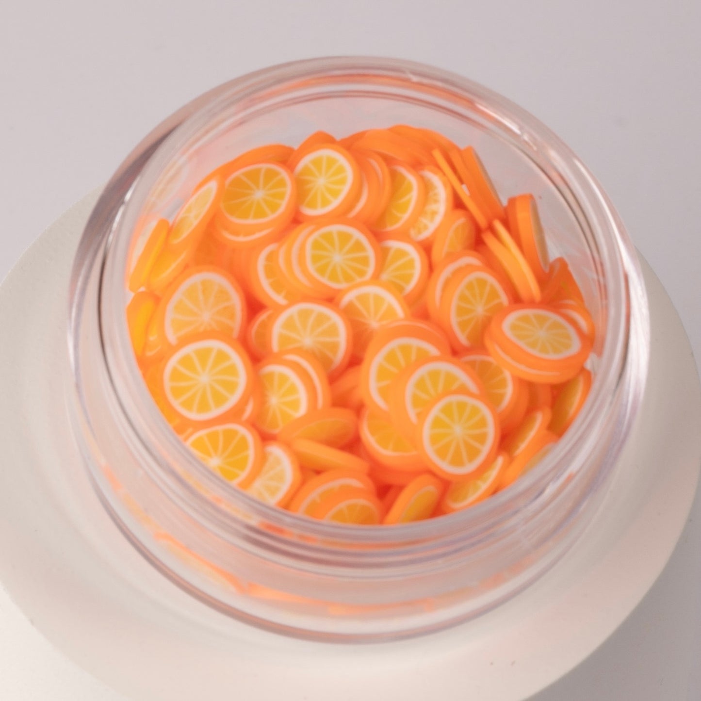 Mini decorative orange slices in clear jar on white background.