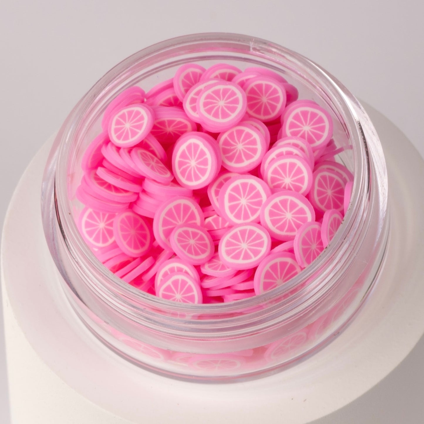 Mini decorative pink lemon slices in clear jar on white background.