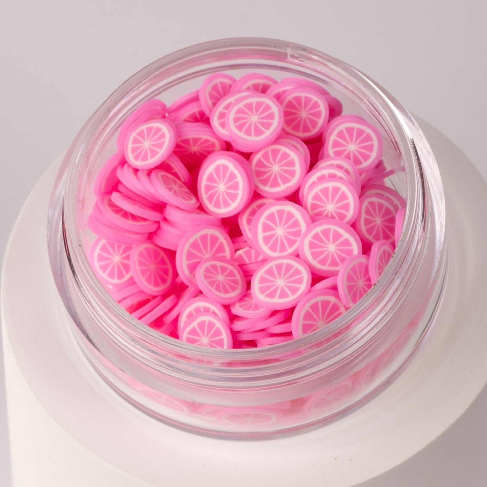 Mini decorative pink lemon slices in clear jar on white background.