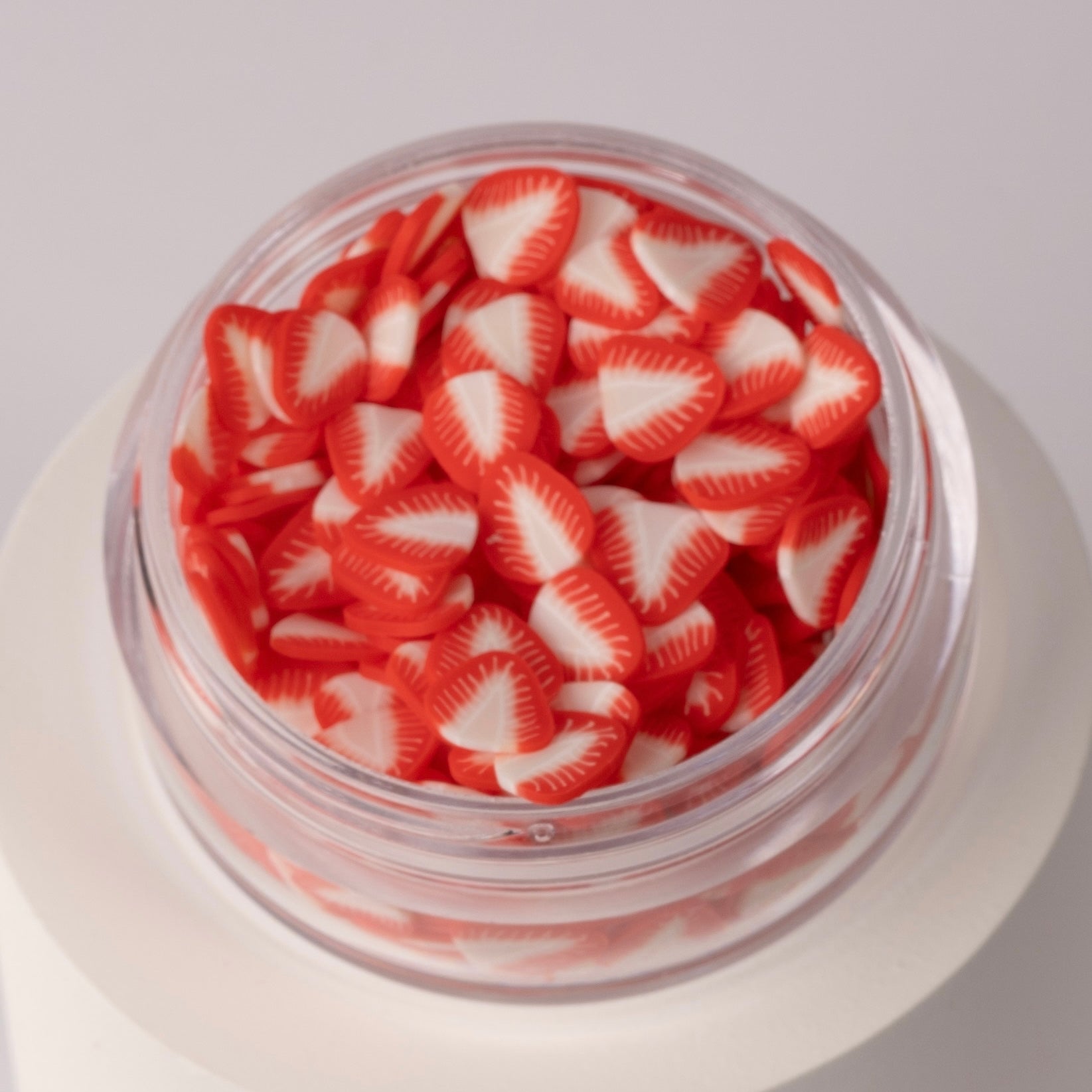 Mini decorative strawberry slices in clear jar on white background.