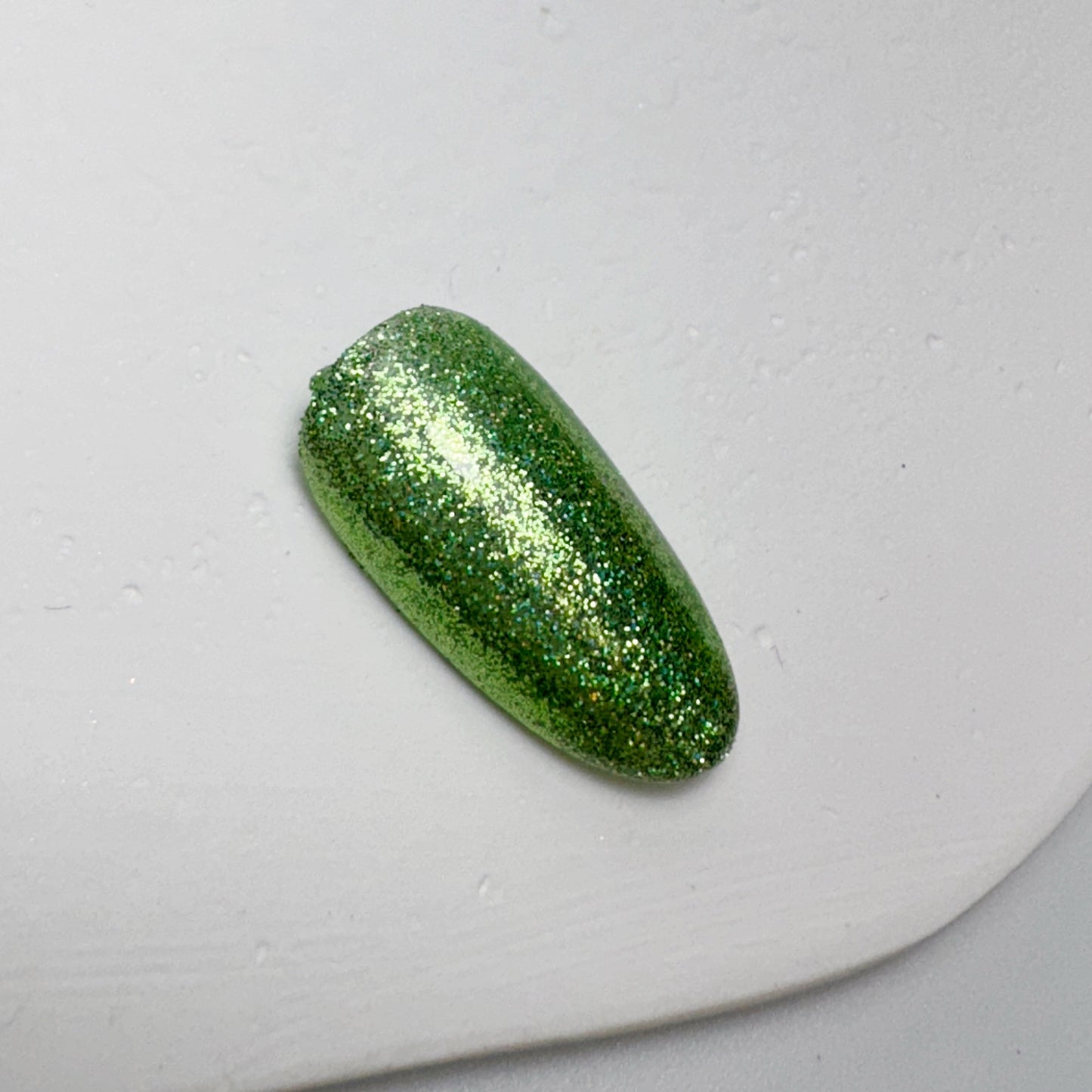 Nail tip with glittery finish on white textured surface.