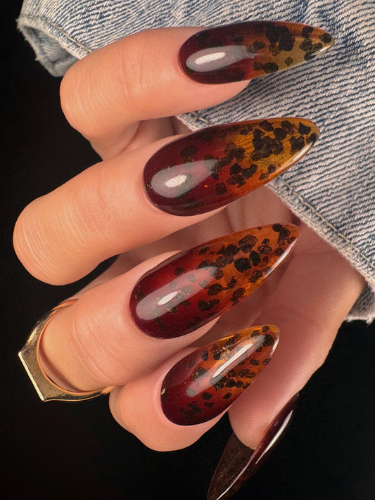 Nail art with sheer brown design and black speckles on a dark background