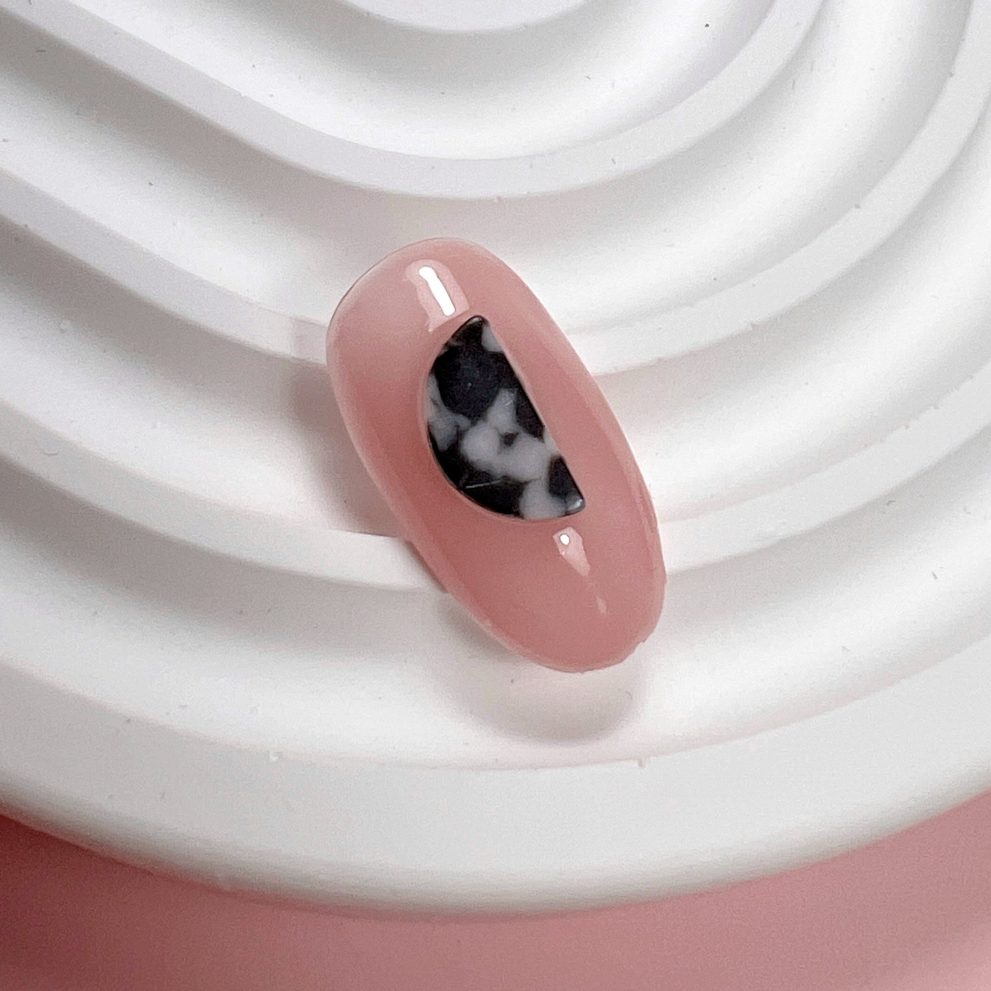 Decorated pink nail tip on white textured surface and pink background.