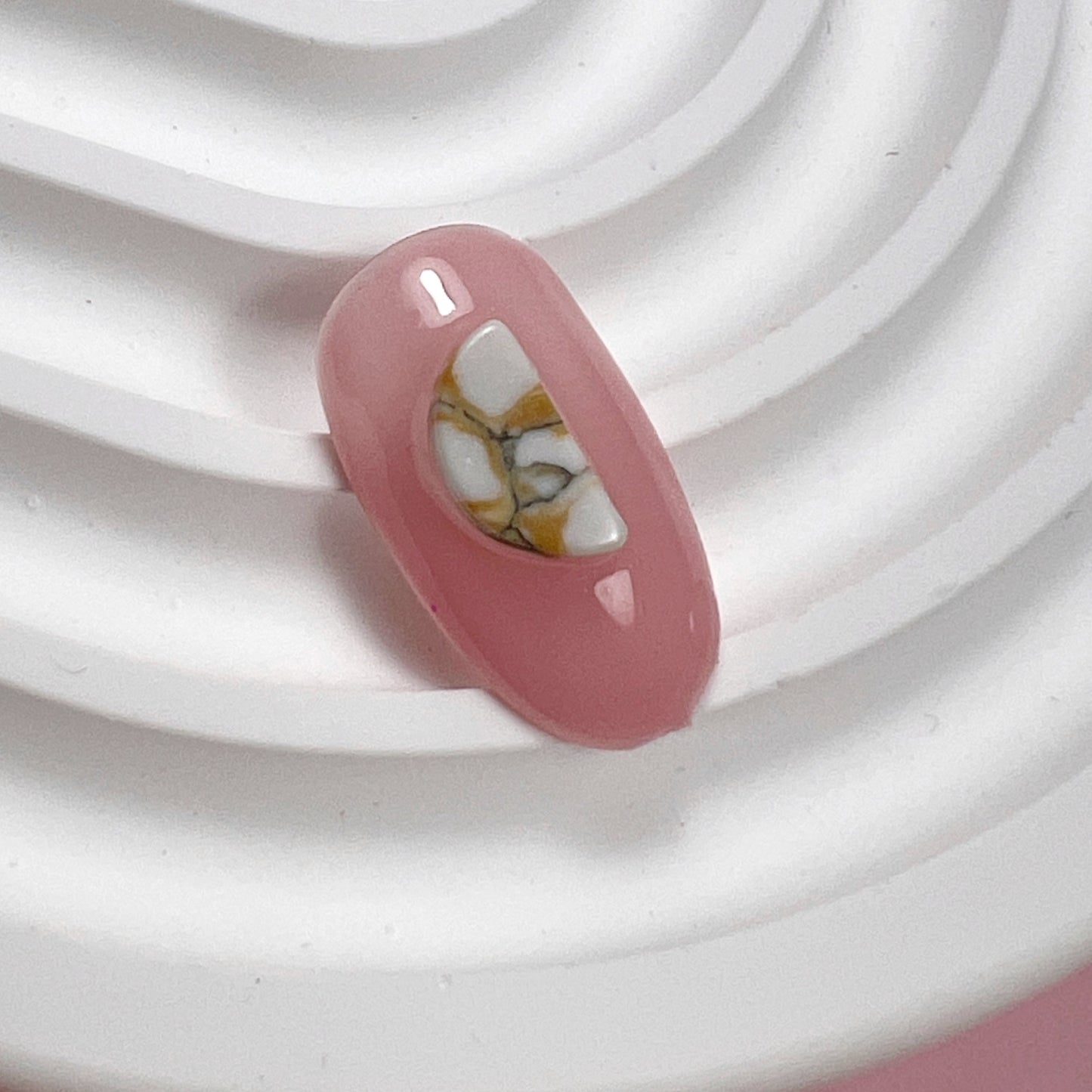 Decorated pink nail tip on white textured surface and pink background.
