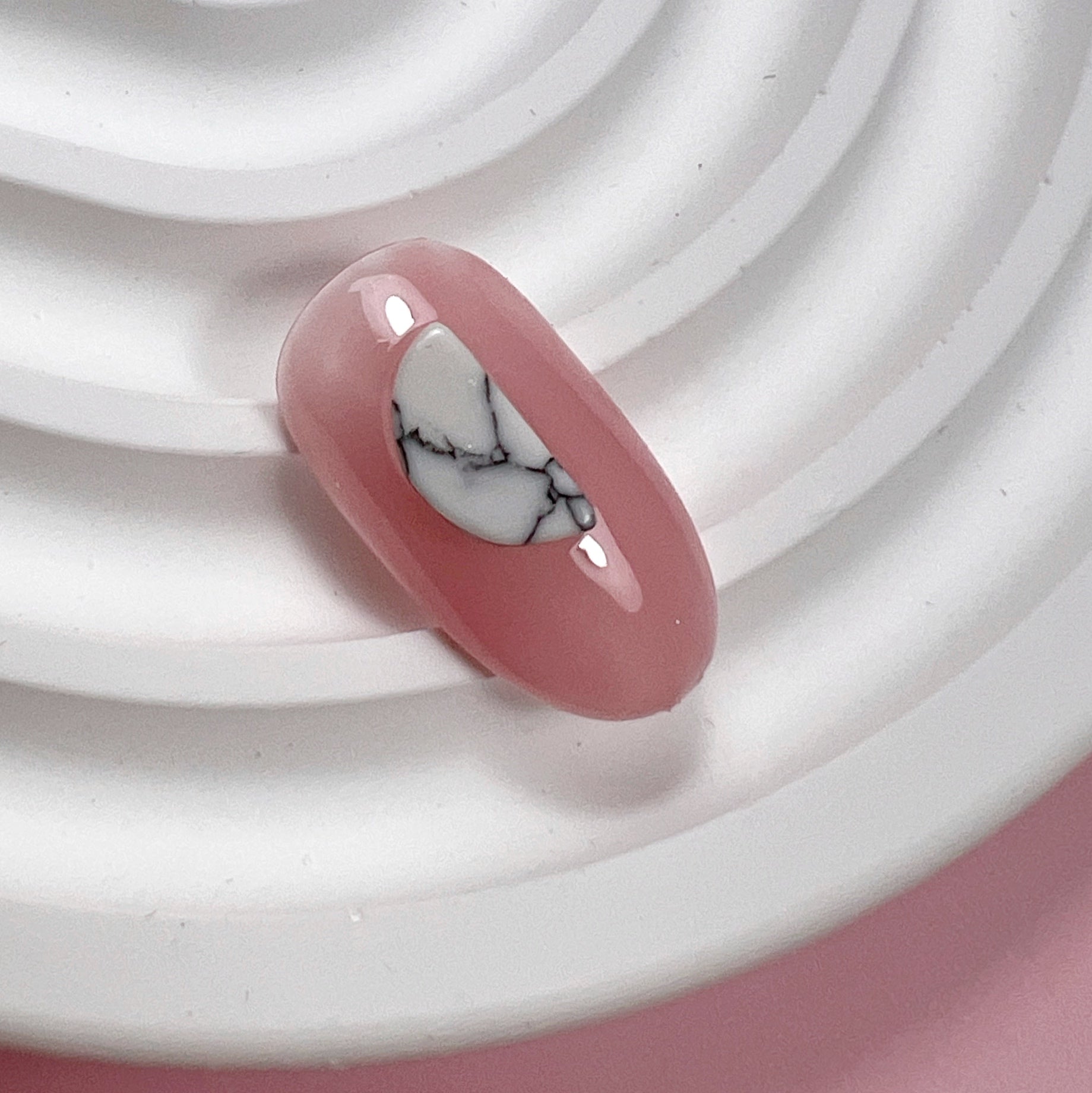 Decorated pink nail tip on white textured surface and pink background.