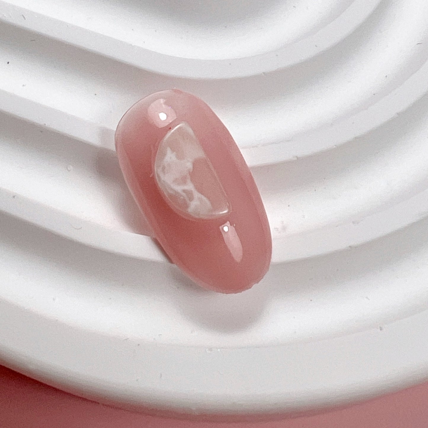 Decorated pink nail tip on white textured surface and pink background.
