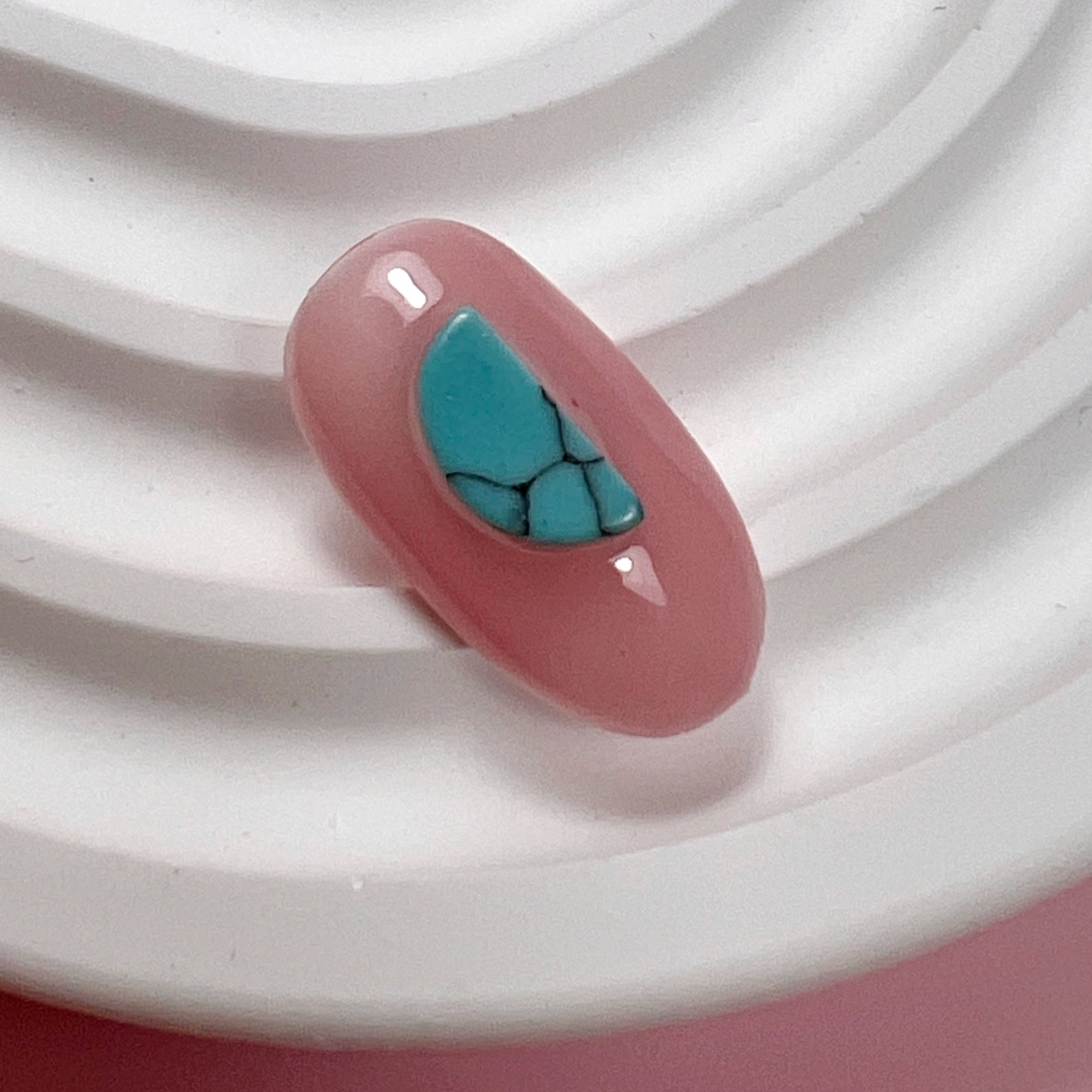 Decorated pink nail tip on white textured surface and pink background.
