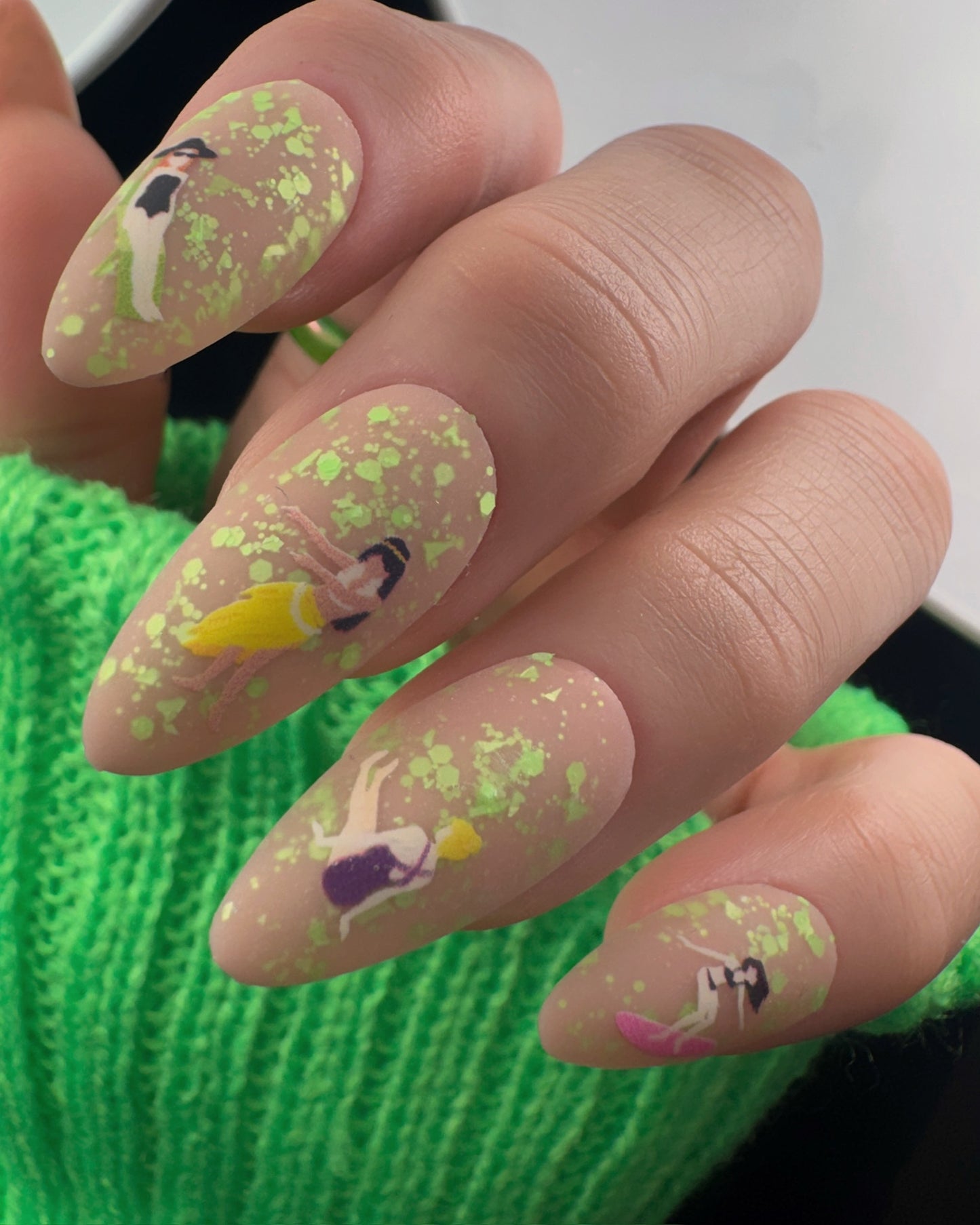 Nails with cartoon character designs and green glitter on a green textured background