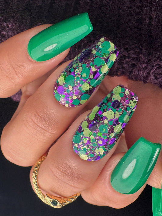 Close-up of a hand with green and multicolored glittery nail polish on a dark background