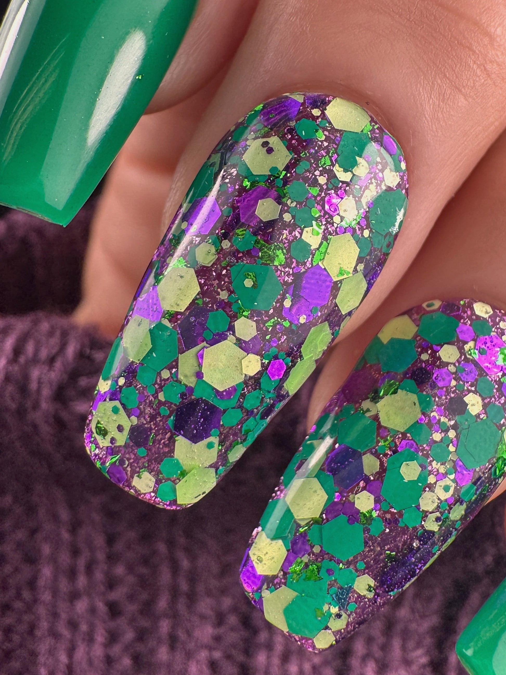 Nail art with green and purple glitter on a textured surface