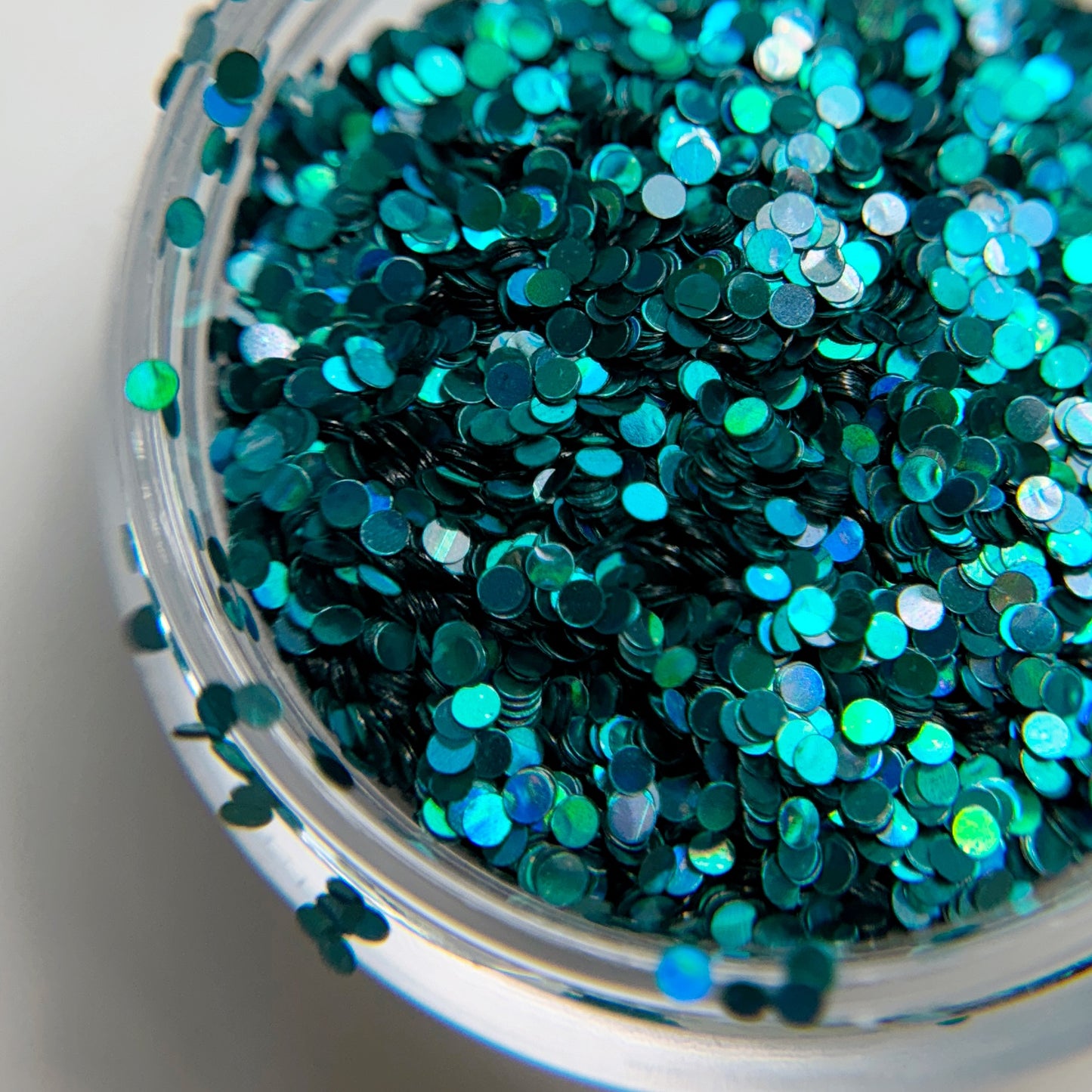 A close-up view of a container filled with teal-colored holographic nail glitter.