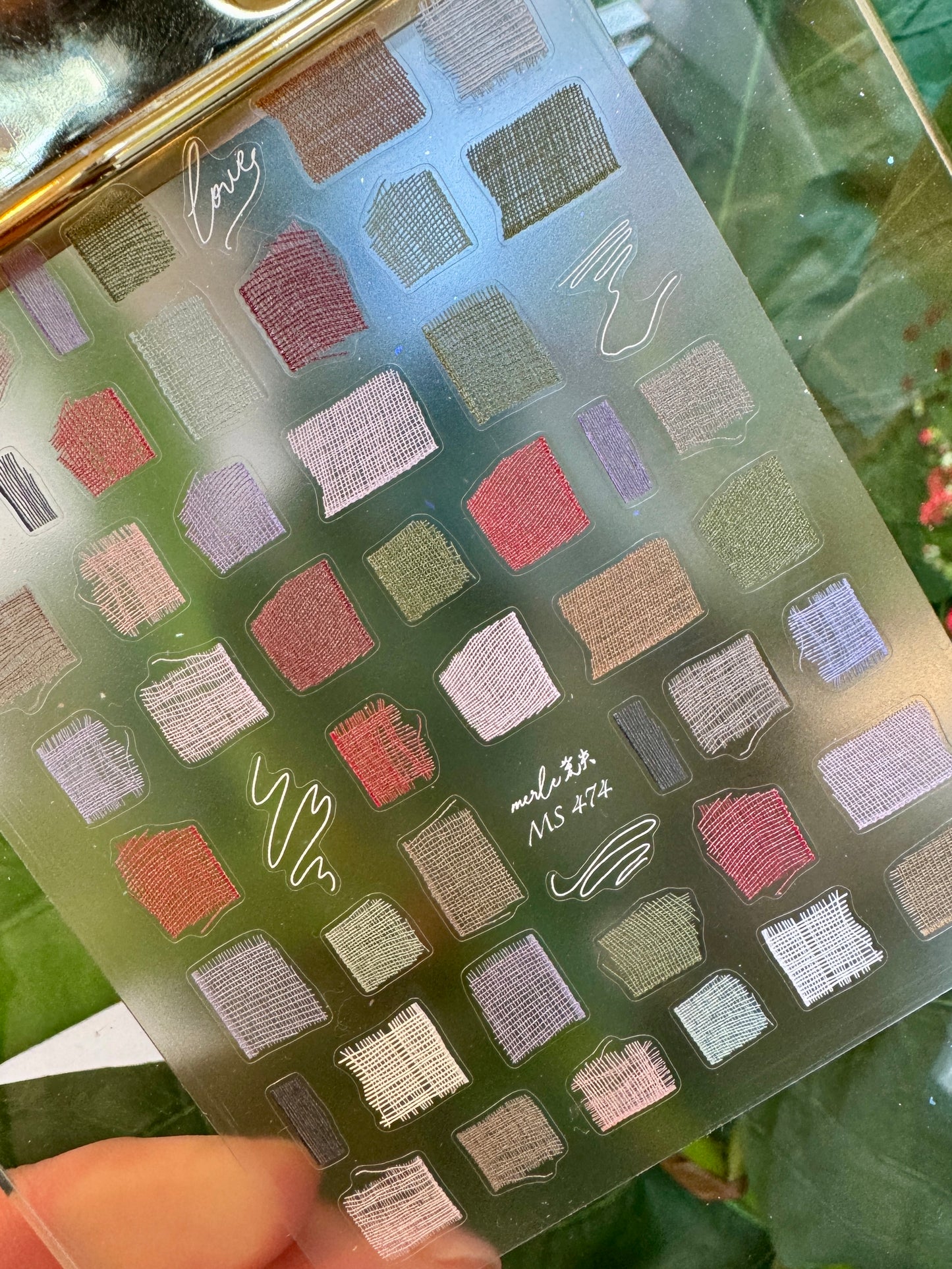 Nail decal sheet with various color swatches on a green leaf background