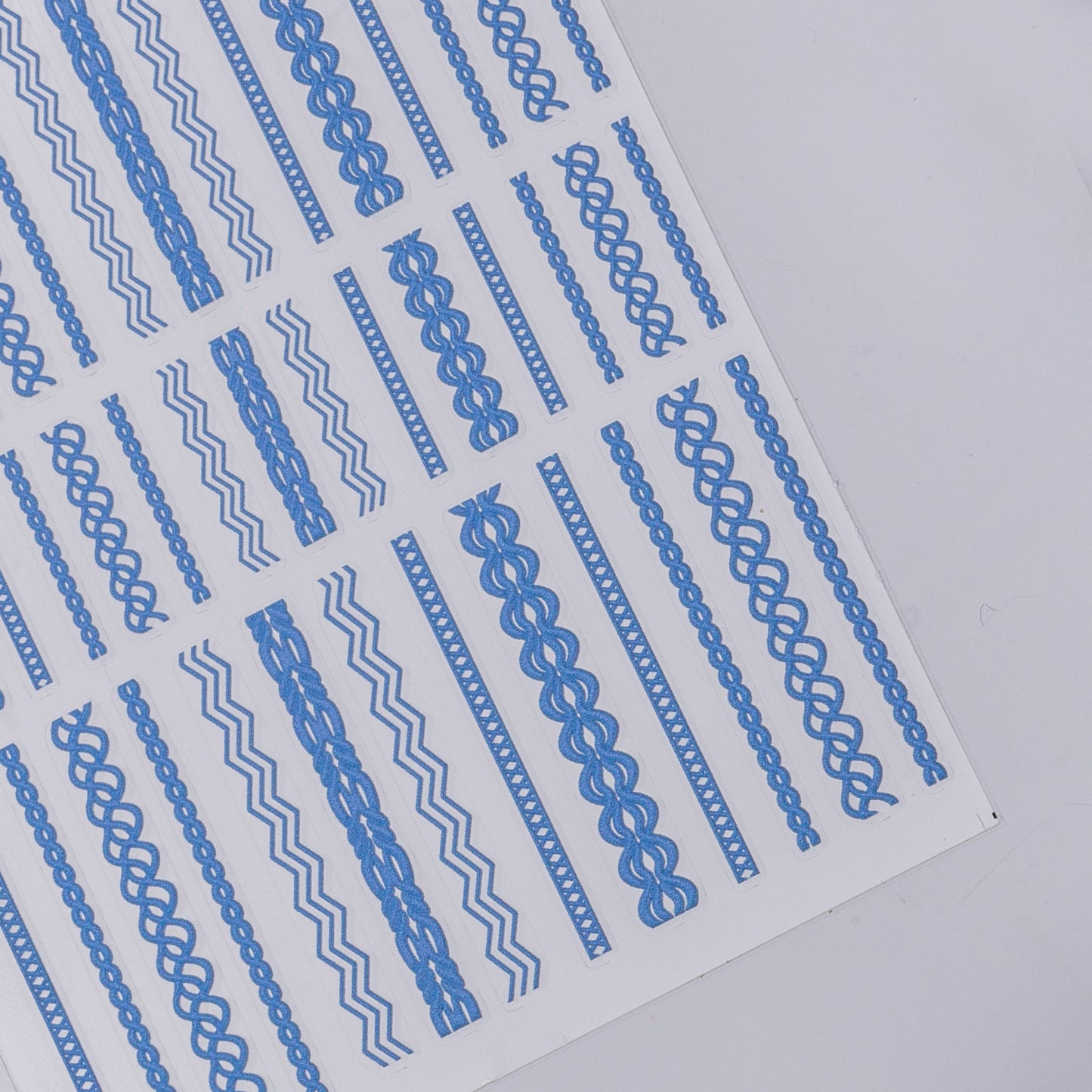 Detail view of nail decal sheet with blue textured stickers on light colored background.