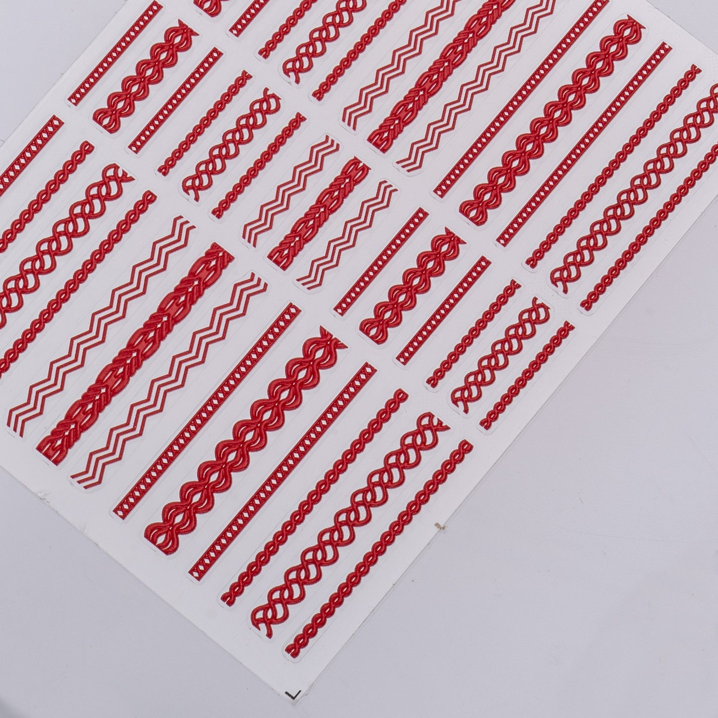 Close up of nail decal sheet with textured red design on light background.
