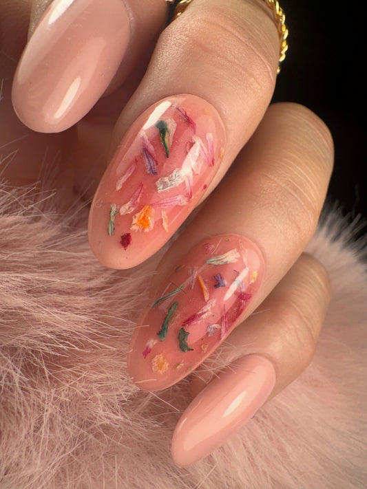 Nail art with floral petal design on a pink background