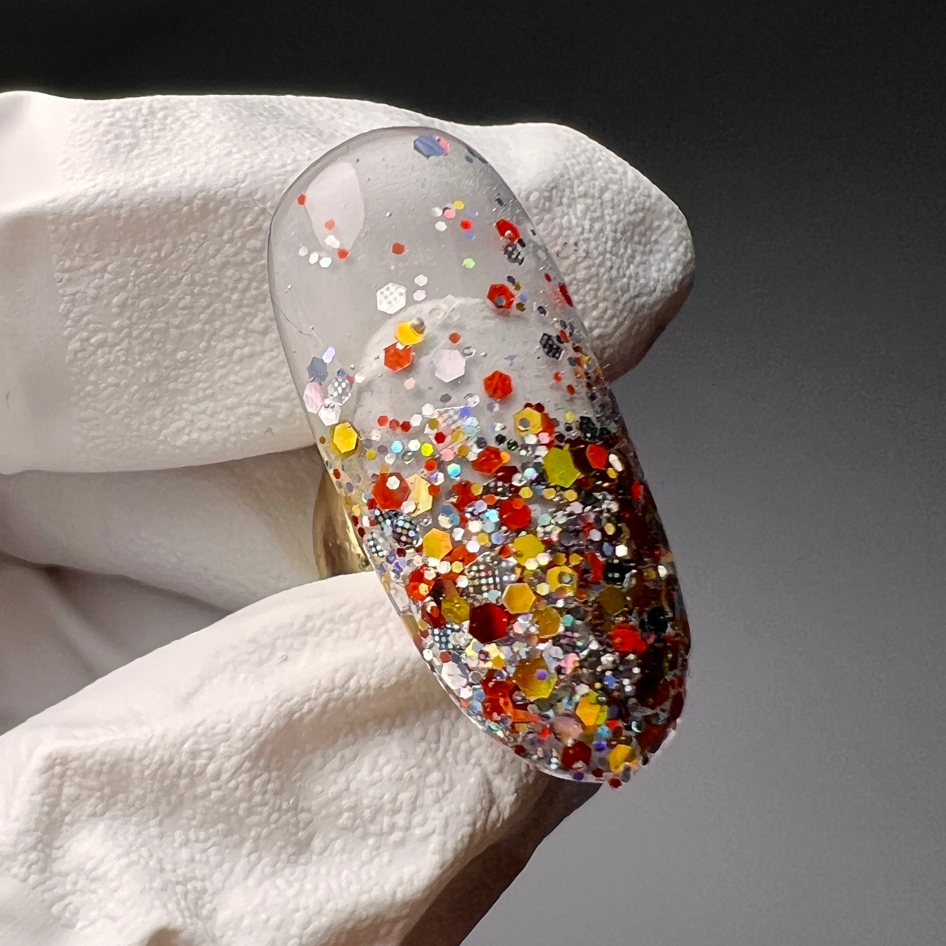 white glove hand holding decorated nail tip on gray background