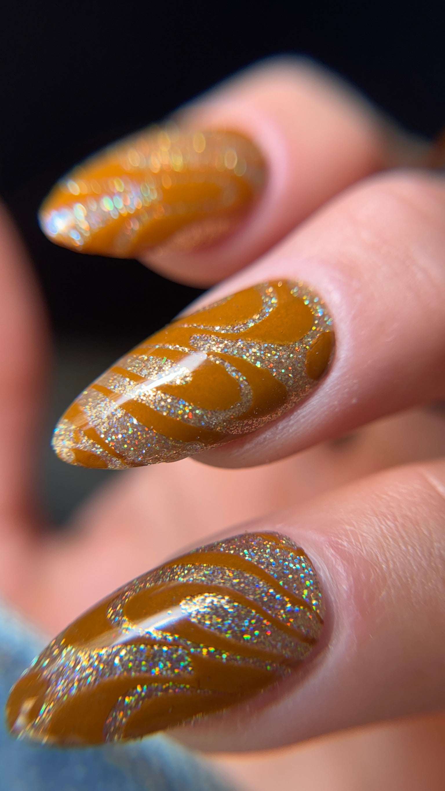 Nails with gold glitter and dark yellow design on a blurred background