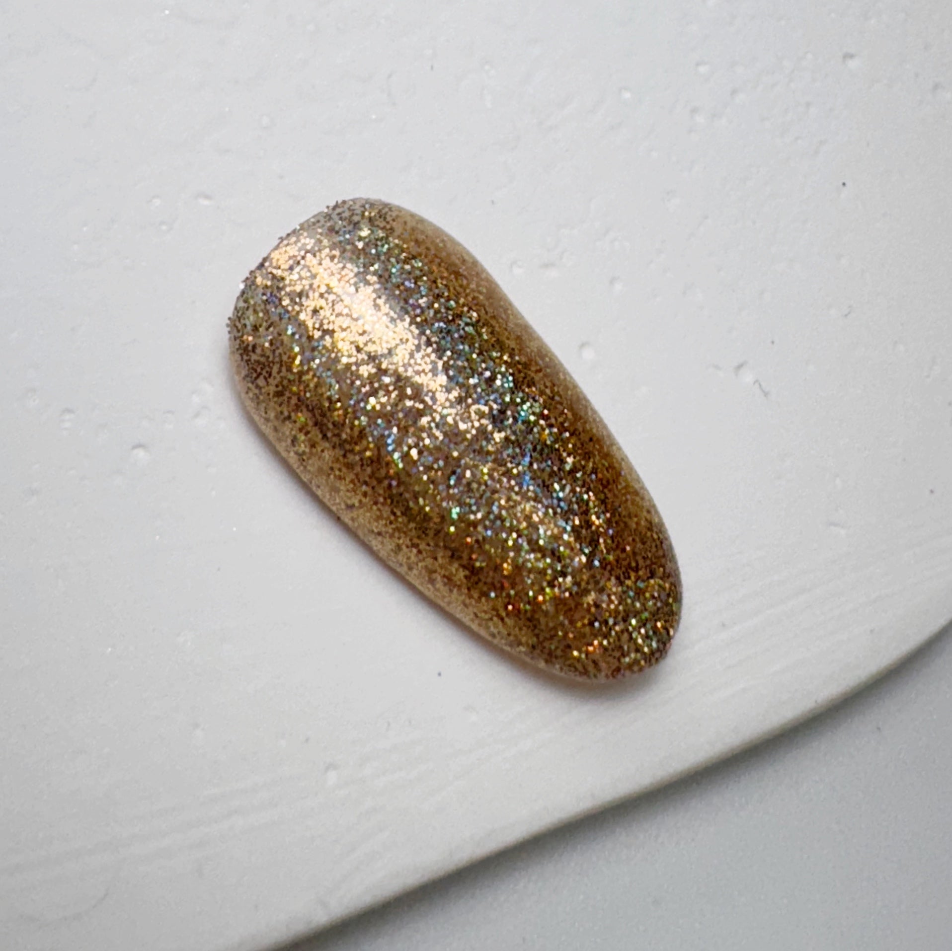 Nail tip with glittery finish on white textured surface.