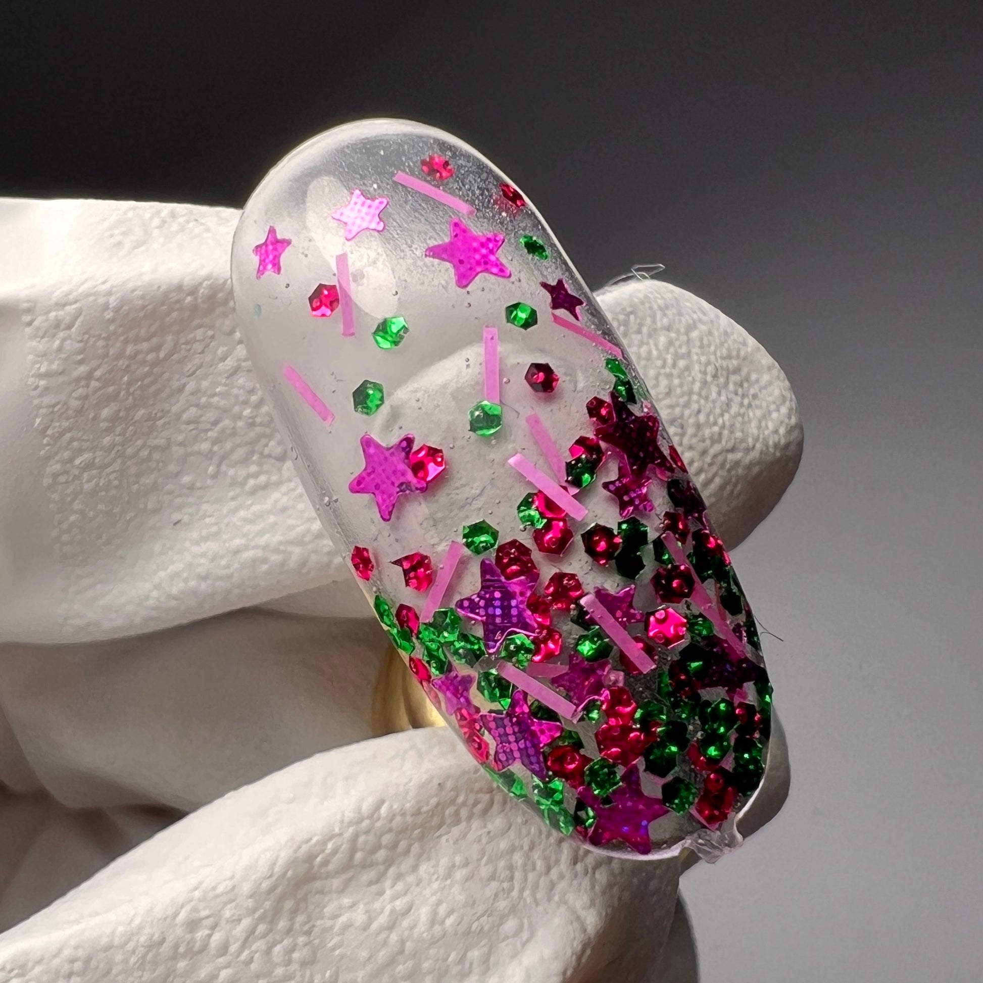 gloved hand holding decorated nail tip on gray background