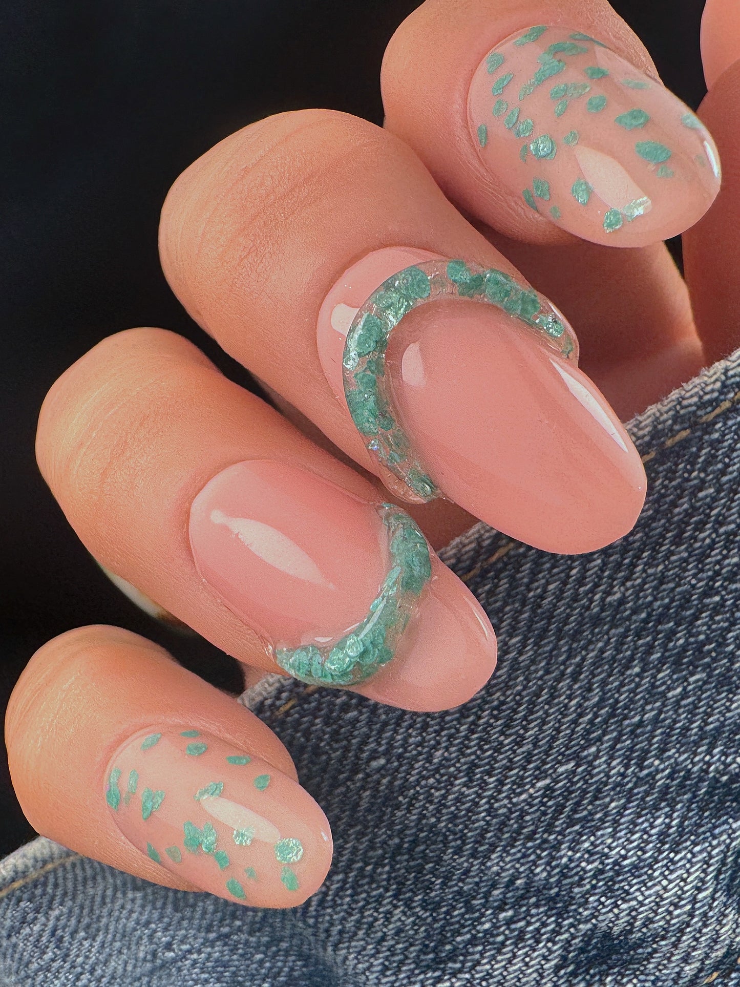Close-up of nails with teal speckled design with clear 3D elements on a denim background