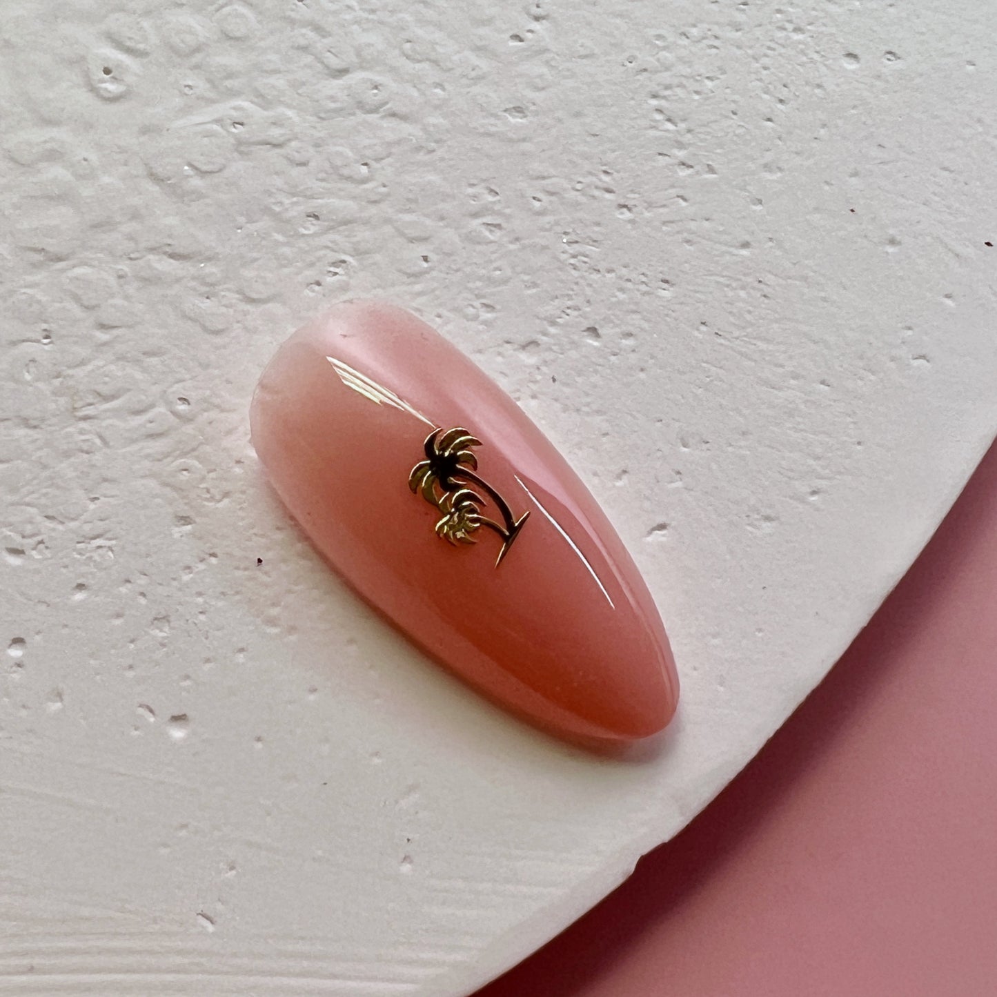 Pink nail with a gold palm tree design on a white background