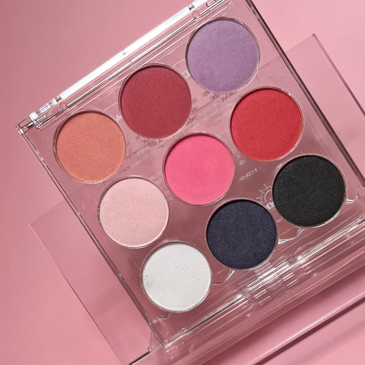 A palette containing various nail powder colors in shades of pink, red, white, navy, and black, displayed on a pink background.