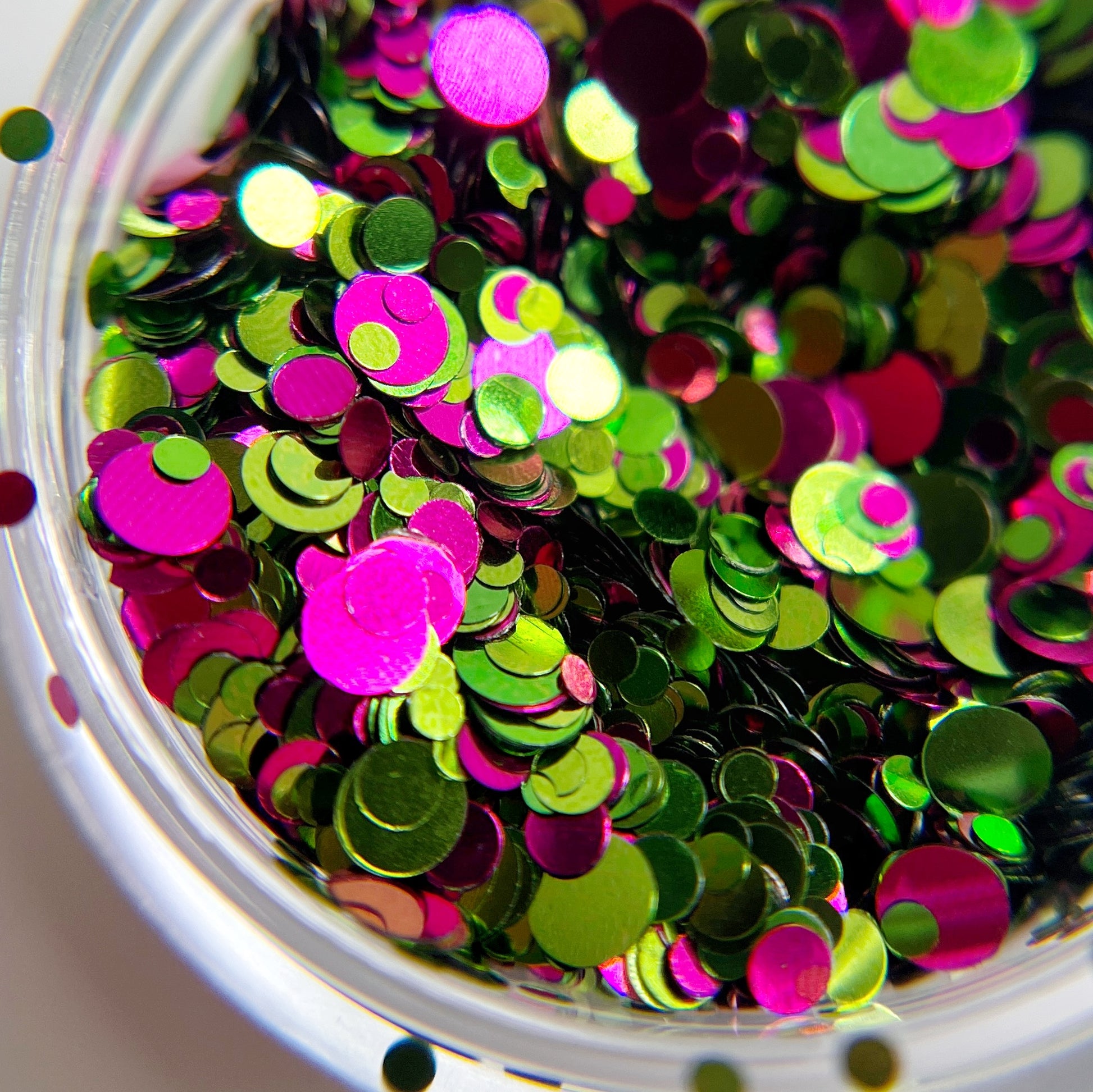 Close up of pink and green round glitter in transparent jar on light background