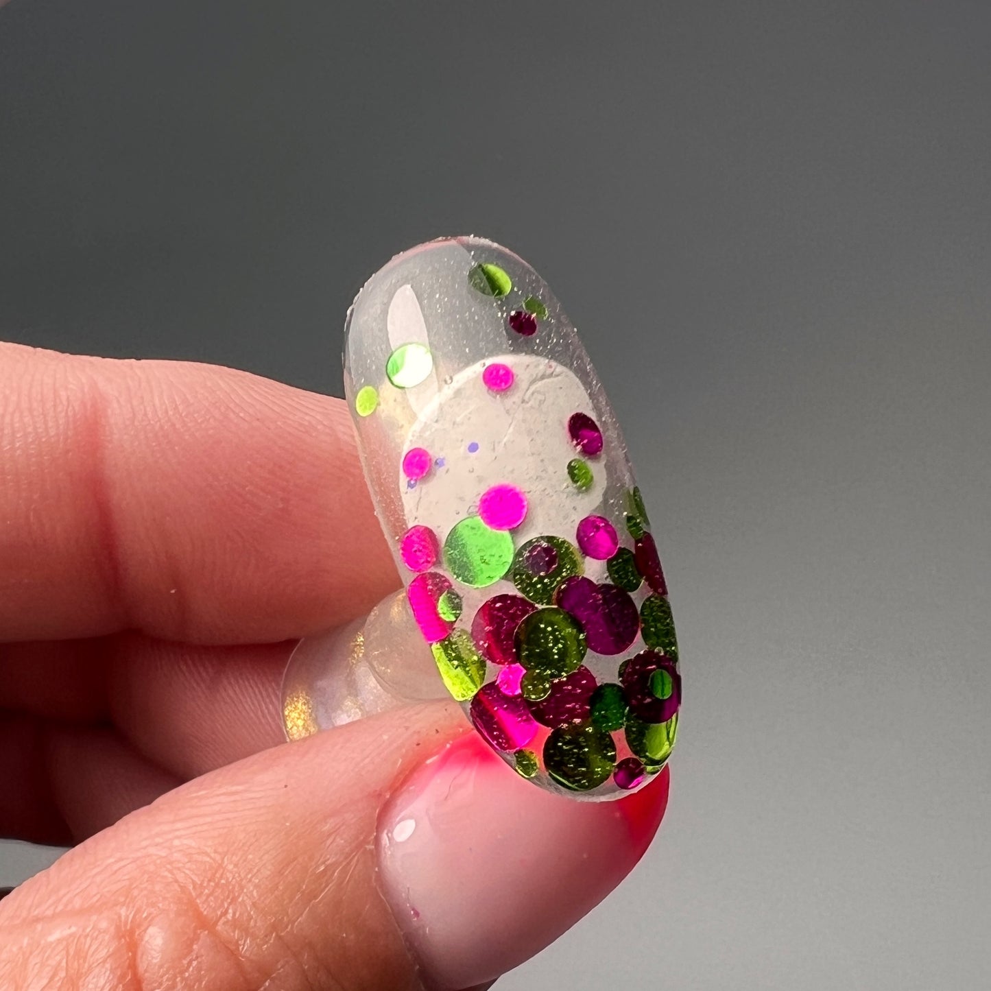 hand holding decorated nail tip on grey background