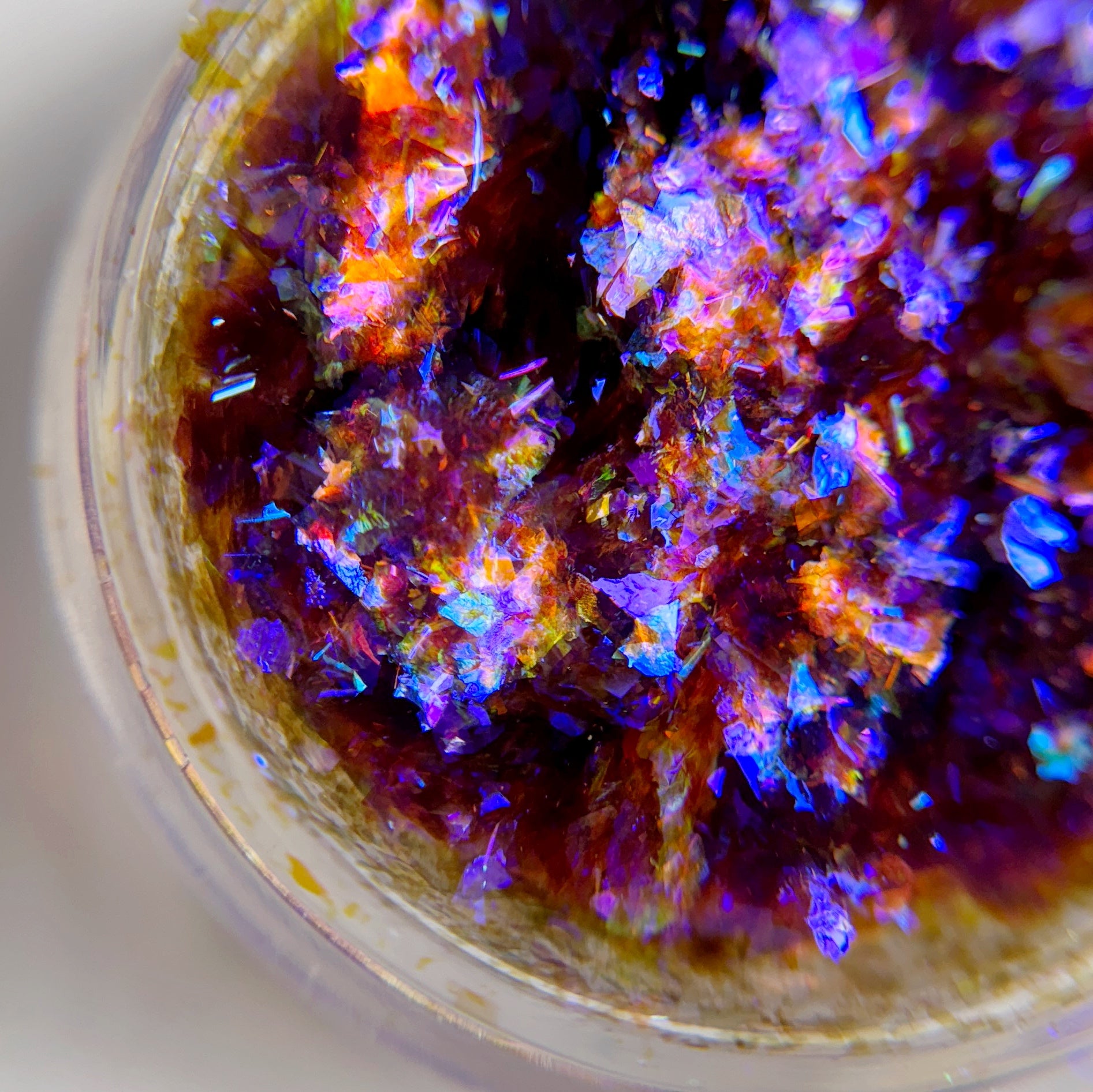 Close up of iridescent flakes in transparent jar on blurred background