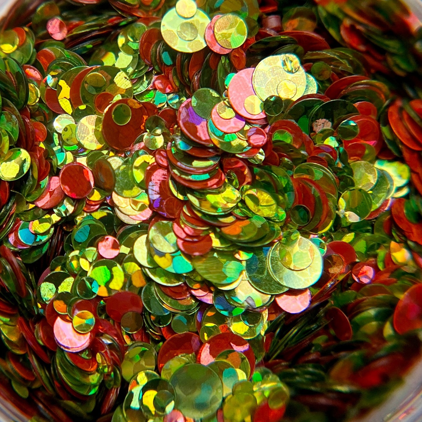 A close-up image of multicolored round glitter pieces, with a mix of pink and green, reflecting light.