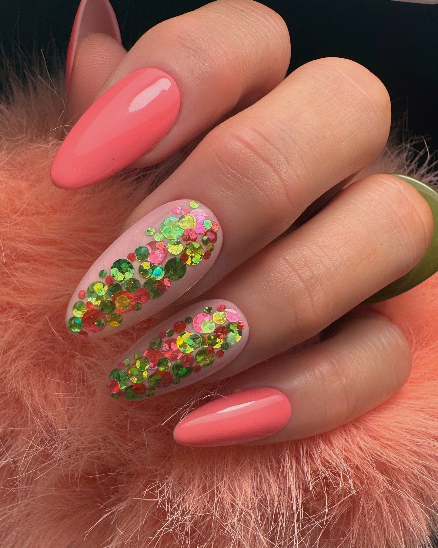 Hand with coral pink nails and glittery design on a fluffy orange surface