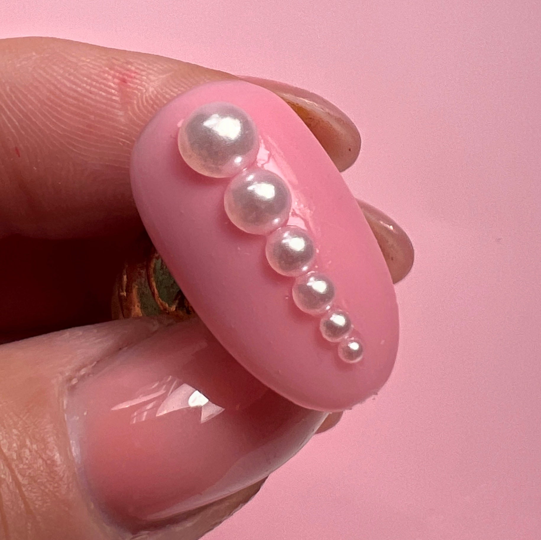 Hand holding decorated nail tip against pink background.