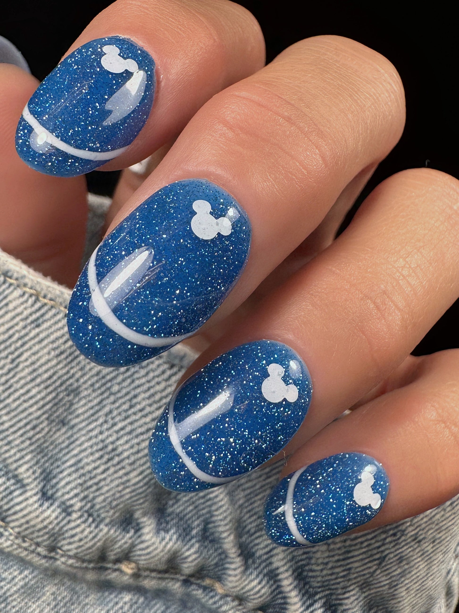 Nails with blue glitter design and white mouse glitter accents on a denim background