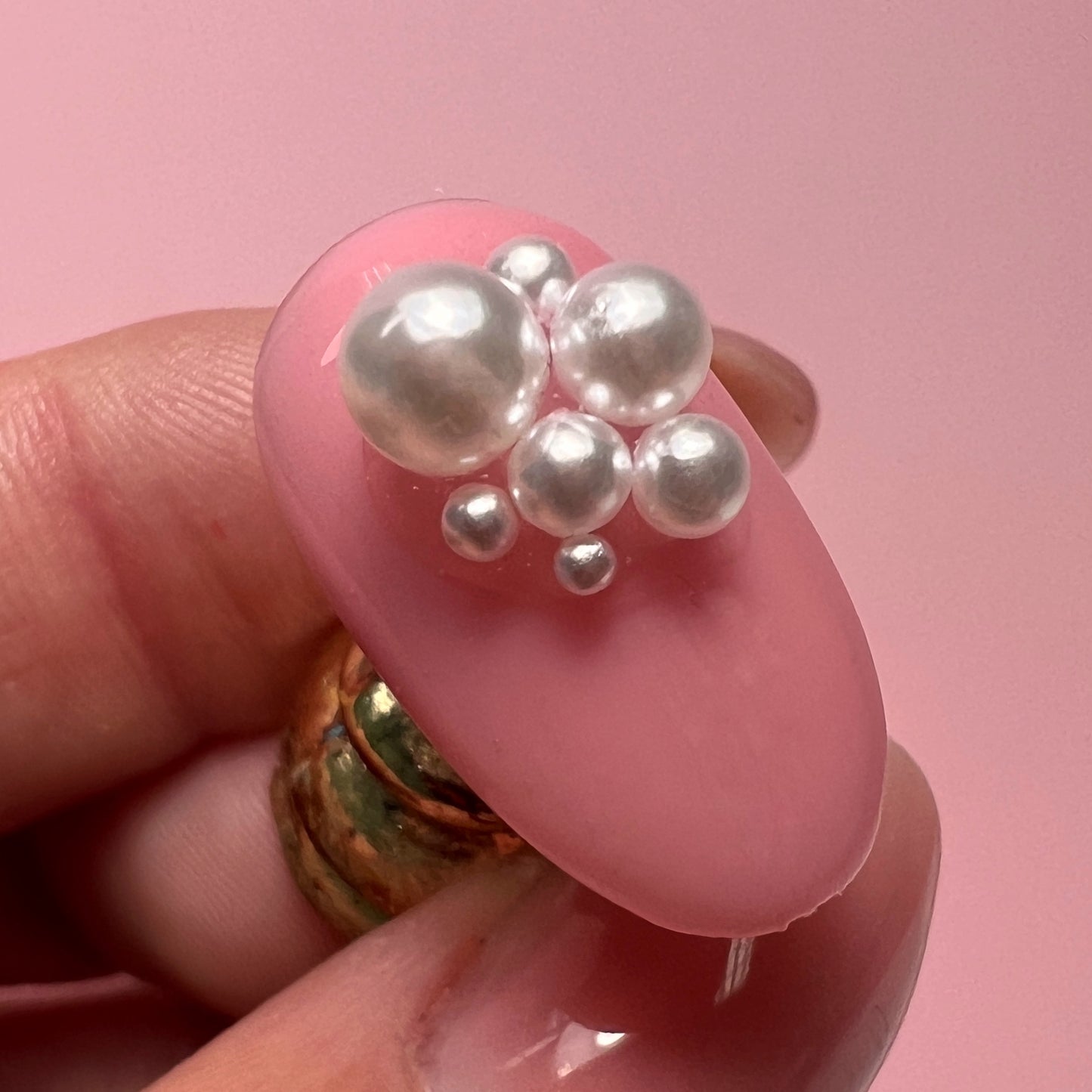Pink nail with pearl decorations held by a hand against a pink background