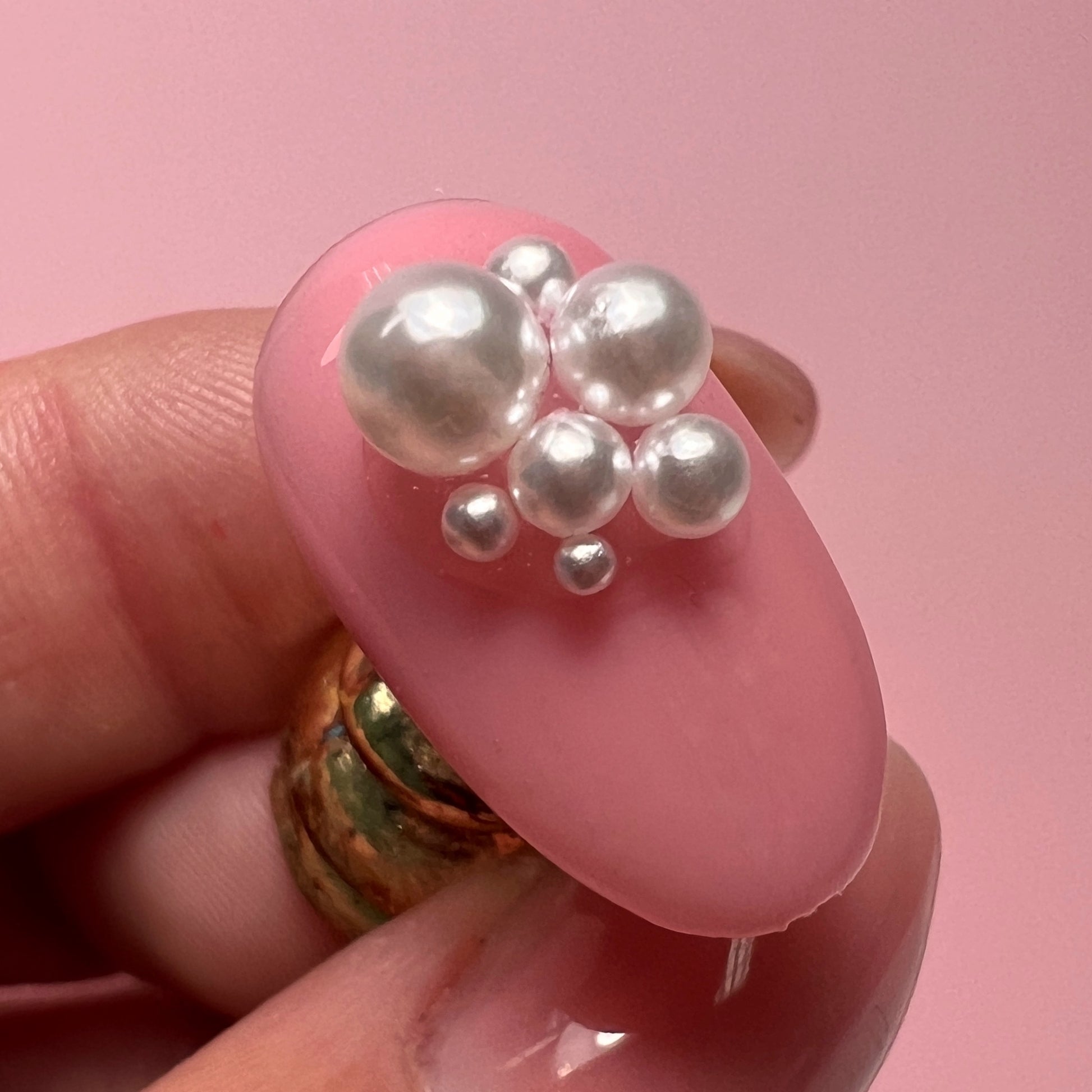Pink nail with pearl decorations held by a hand against a pink background