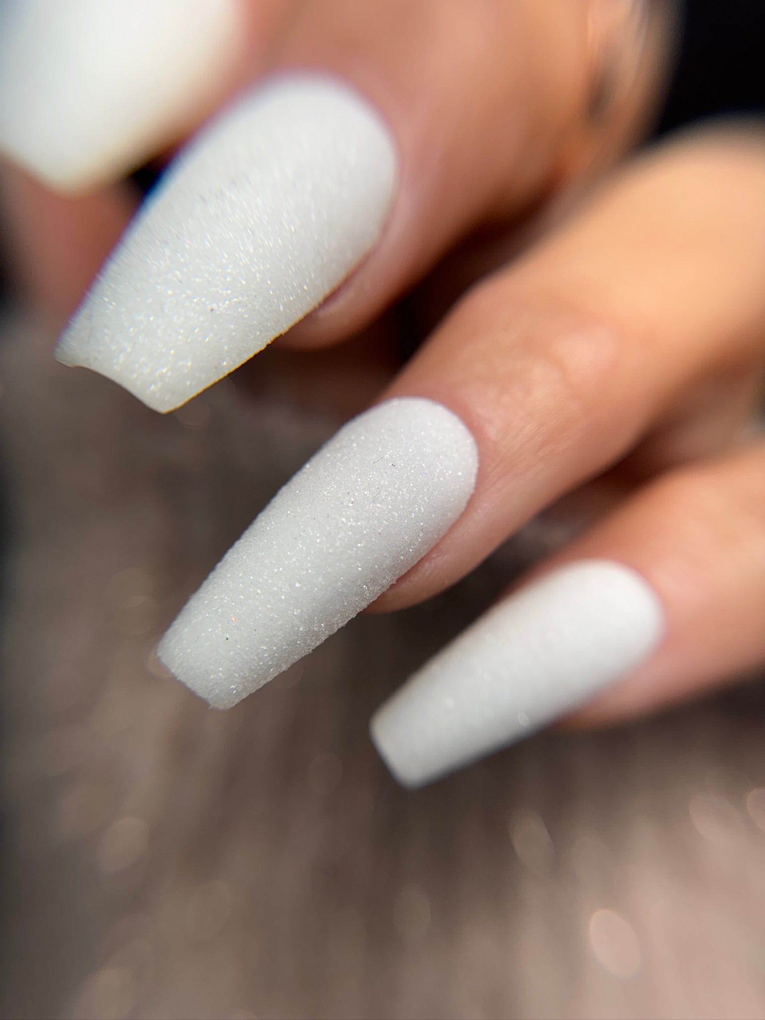 Close-up of a hand with white glitter texture on nails on a blurred background