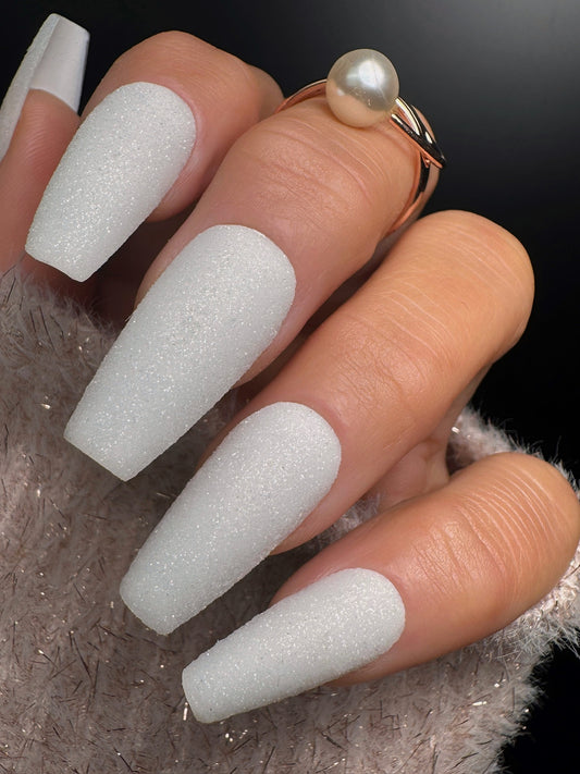 Manicured nails with textured white glitter on a neutral background