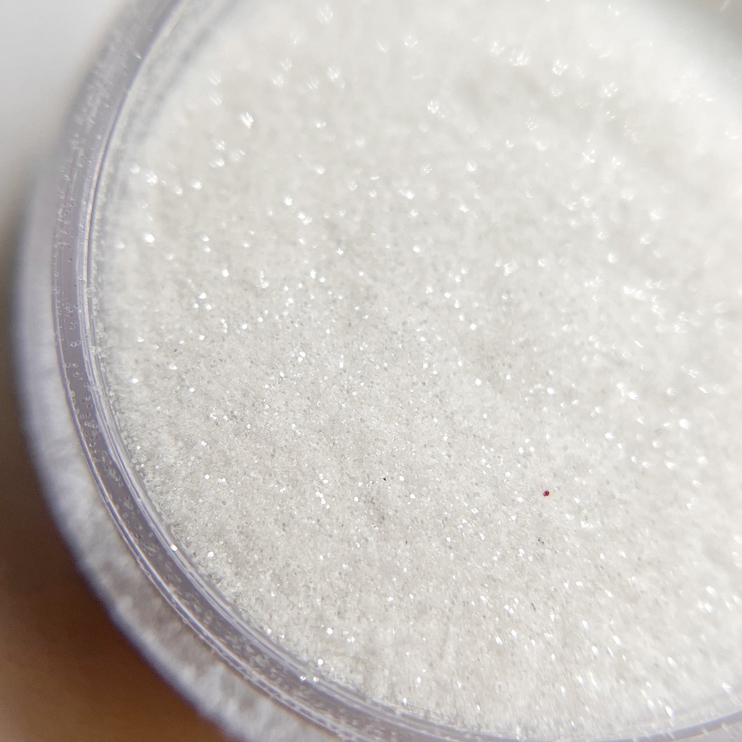Close up of fine glitter in transparent jar on blurred background