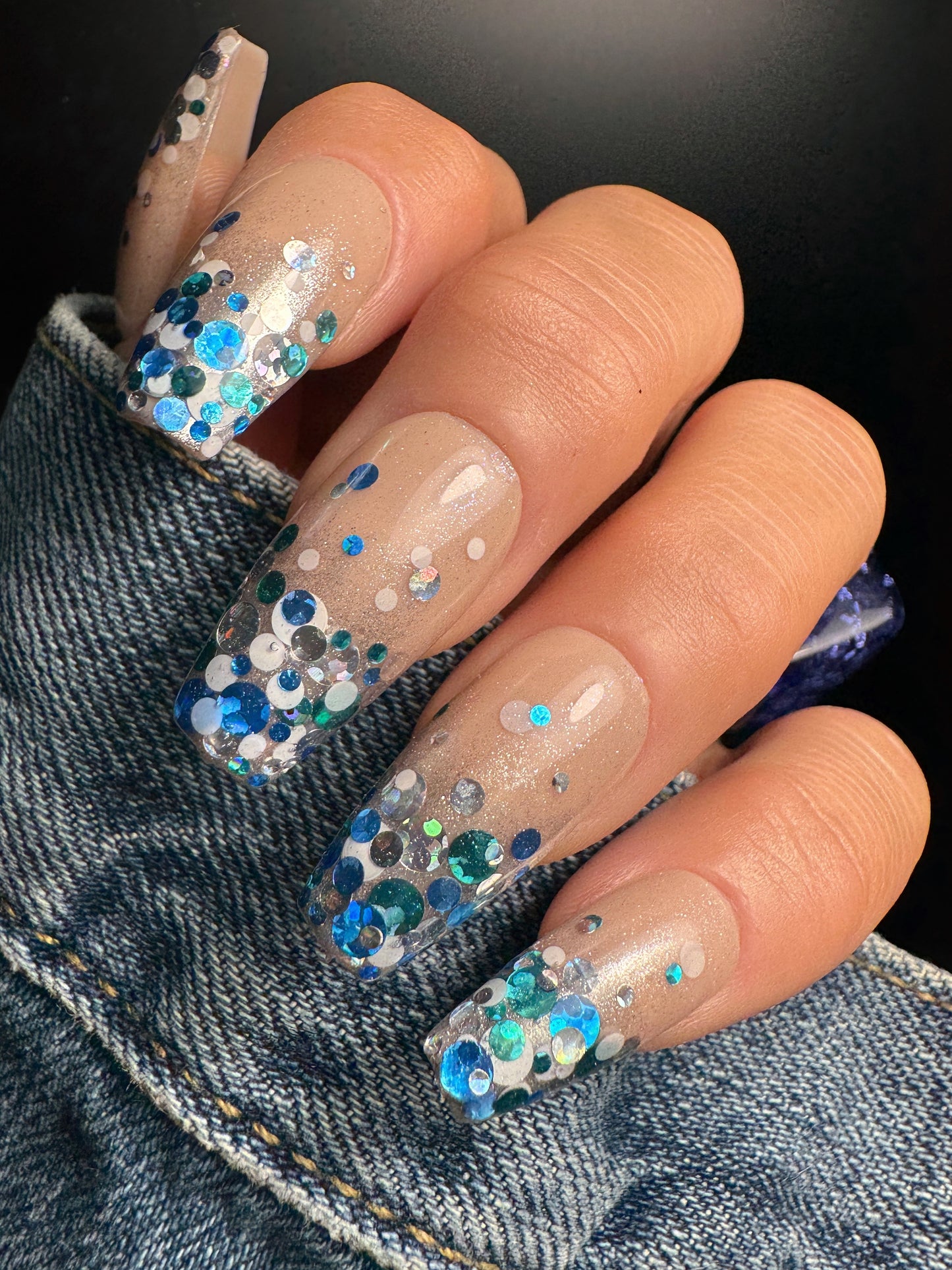 Nails with blue and green glitter design on a denim background