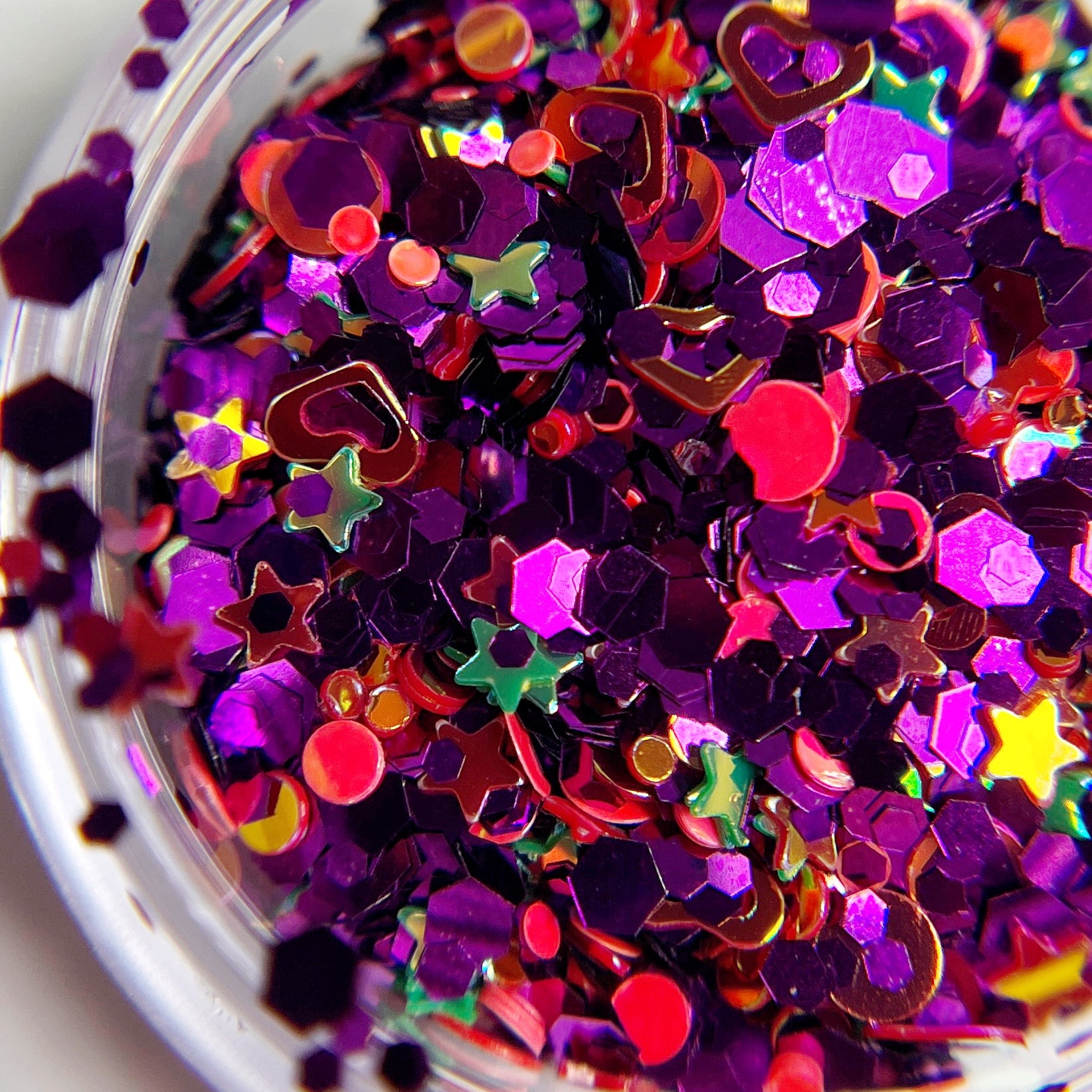 A close-up view of multicolored Witchy Sparkle Glitter, including purple, red, and silver particles with various shapes such as stars and hearts.