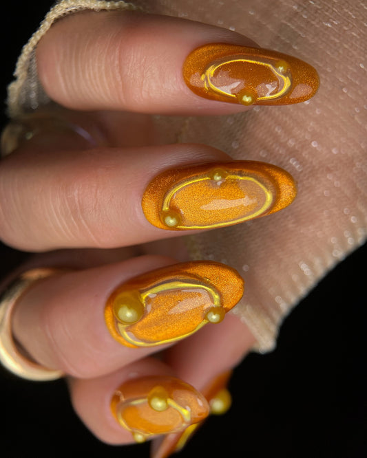 Close-up of a hand with orange nail polish and gold accents.