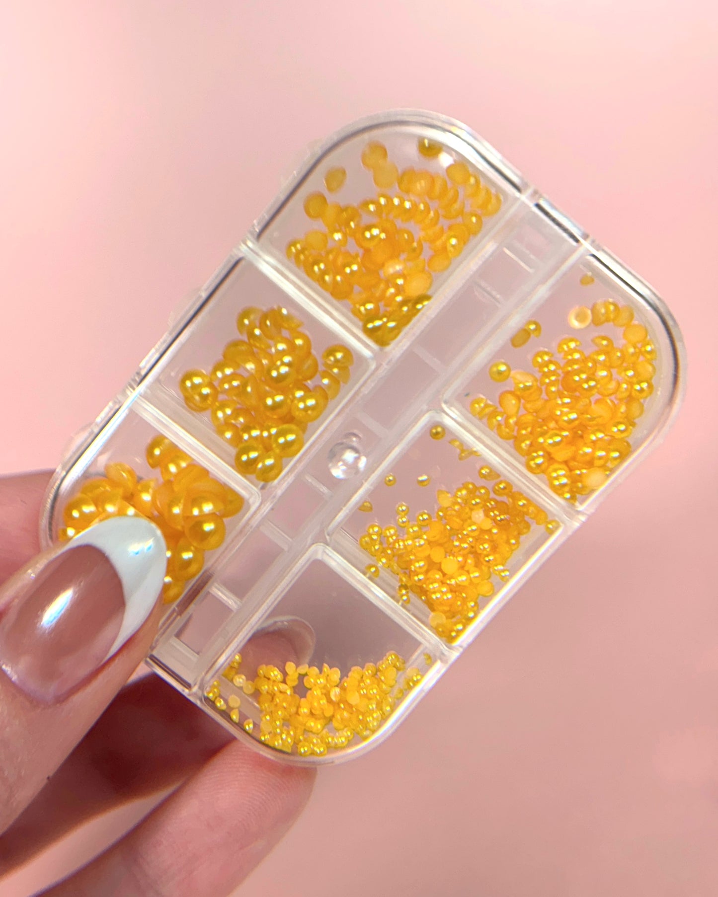 Small container filled with yellow pearly half-sphere beads held by a hand against a pink background
