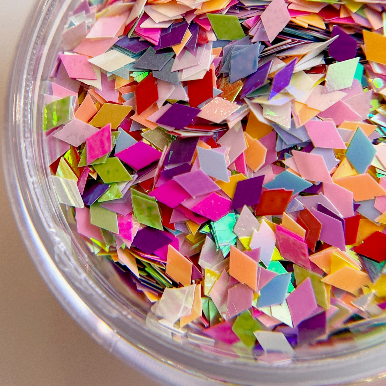 Multicolor diamond shape glitter mix in clear jar on white background. 
