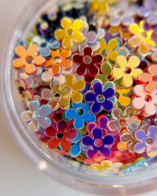 Detail view flower shaped nail glitter in clear jar on white background