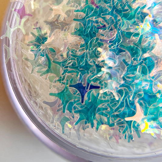 iridescent four point star shaped glitter in a clear jar on a white background. 