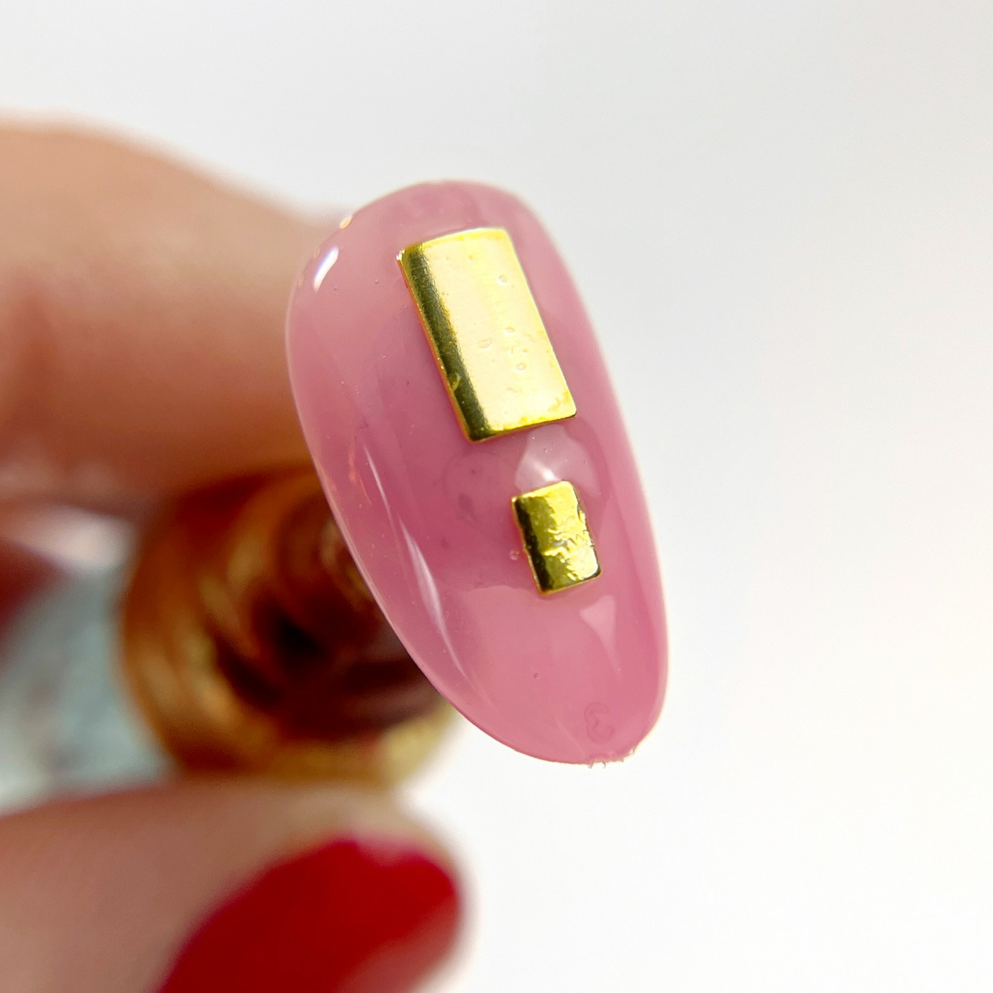 Hand holding nail tip with gold rectangle charms. 