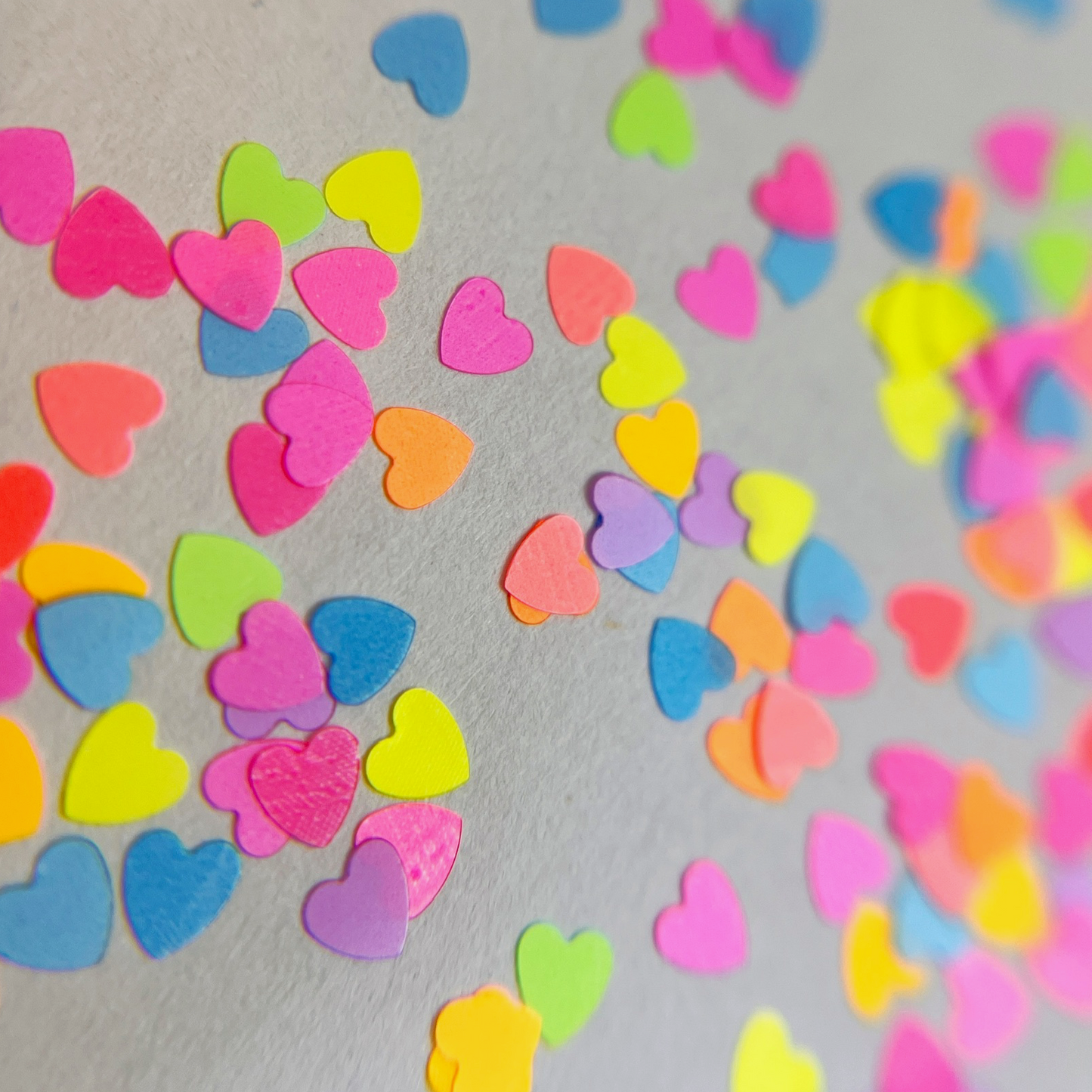 Multi-color heart shaped glitter scattered on white background.