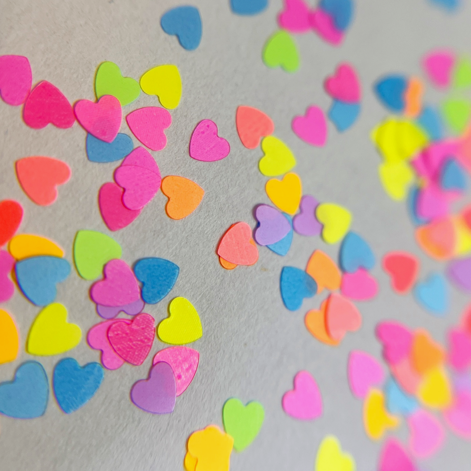 Multi-color heart shaped glitter scattered on white background.