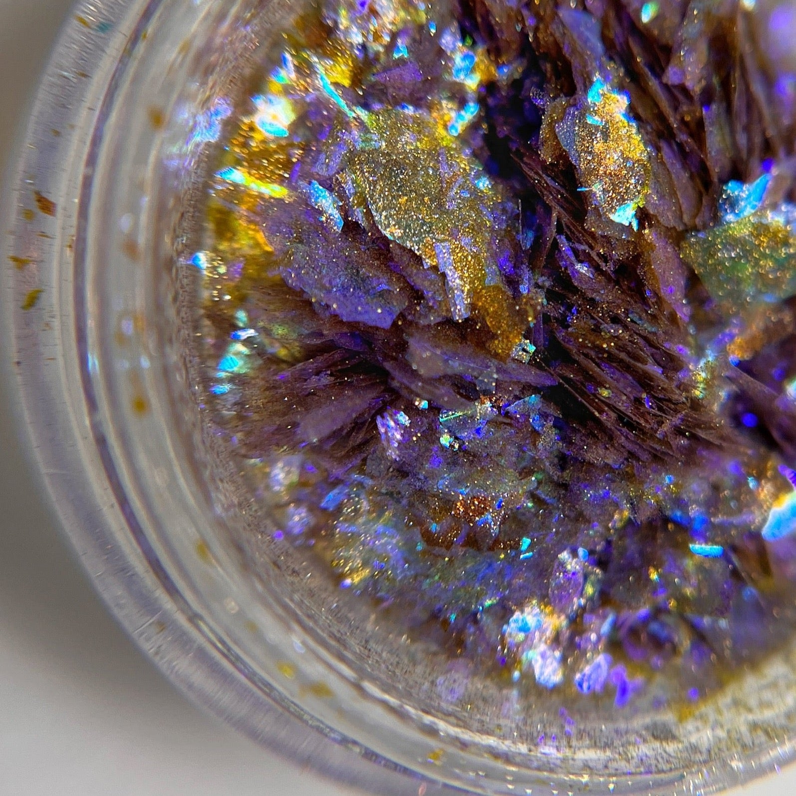 Close up image of iridescent blue flakes in transparent jar on light background